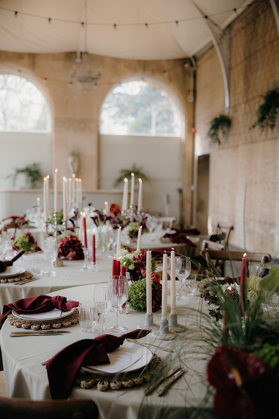 A wedding breakfast set up with green and burgundy floral arrangement, personalised white menu and name places and candles