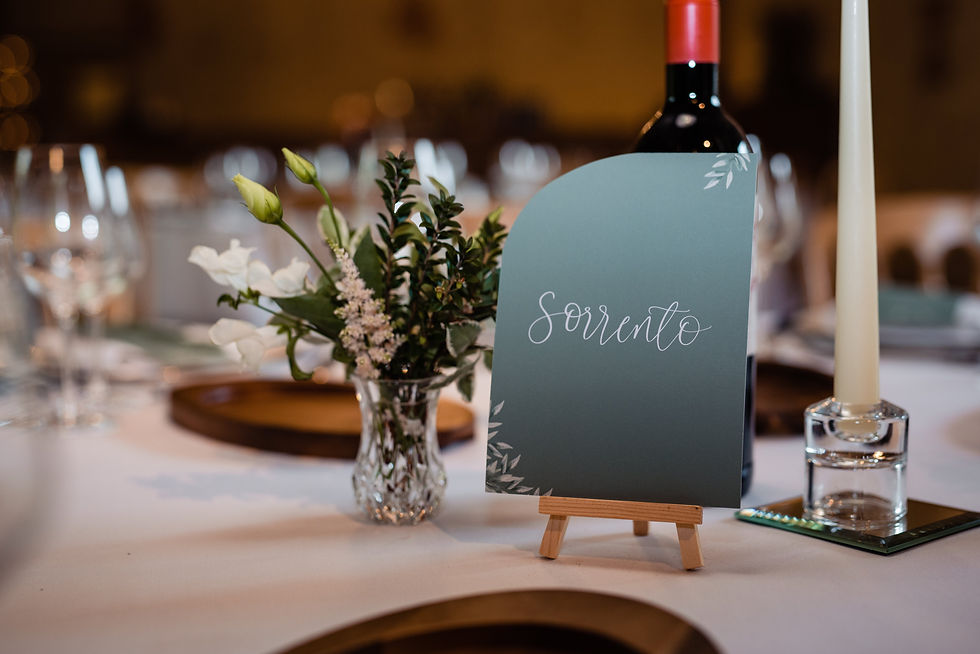 A wedding table number personalised with white calligraphy on a teal background with a foliage design in the corners and a curved edge