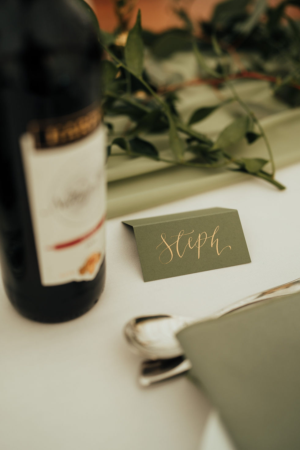 A guest place name personalised with hand drawn calligraphy in gold ink on a green place card