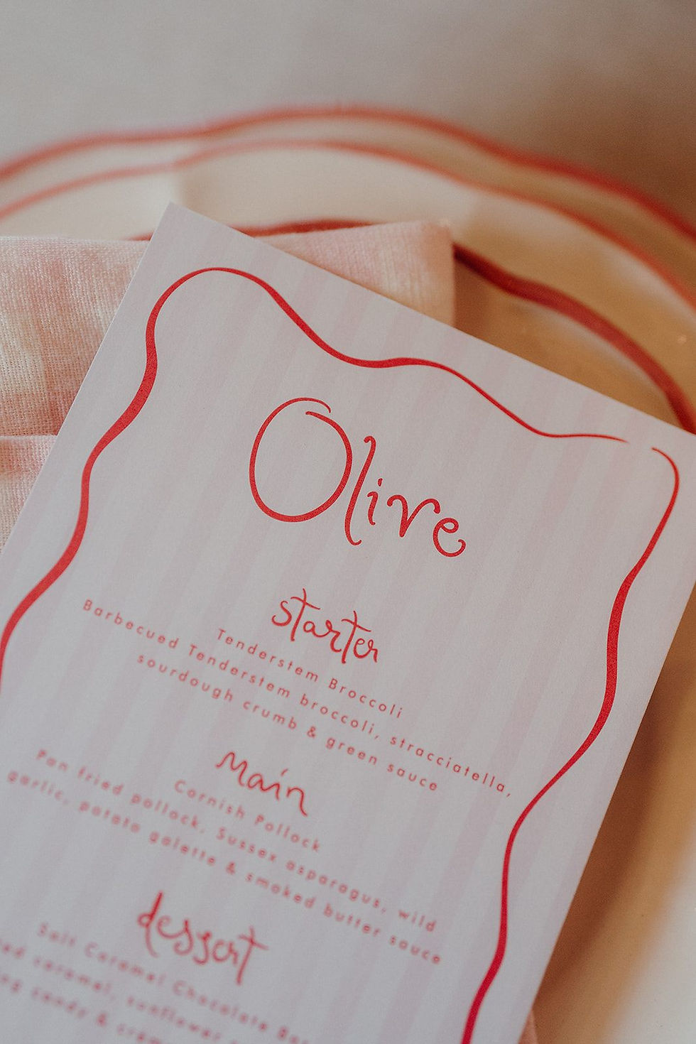 A wedding menu with a pink whimsy calligraphy font, a pink wavy border and pale pink and white striped background