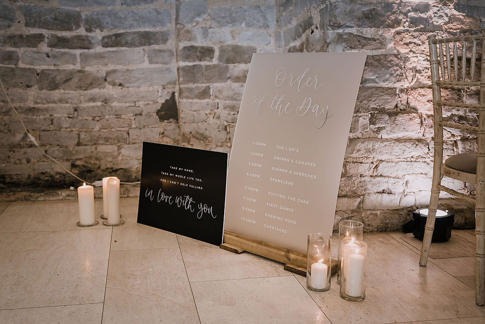 An order of events sign on frosted perspex next to a sign with song lyrics in white text and calligraphy on a black background.