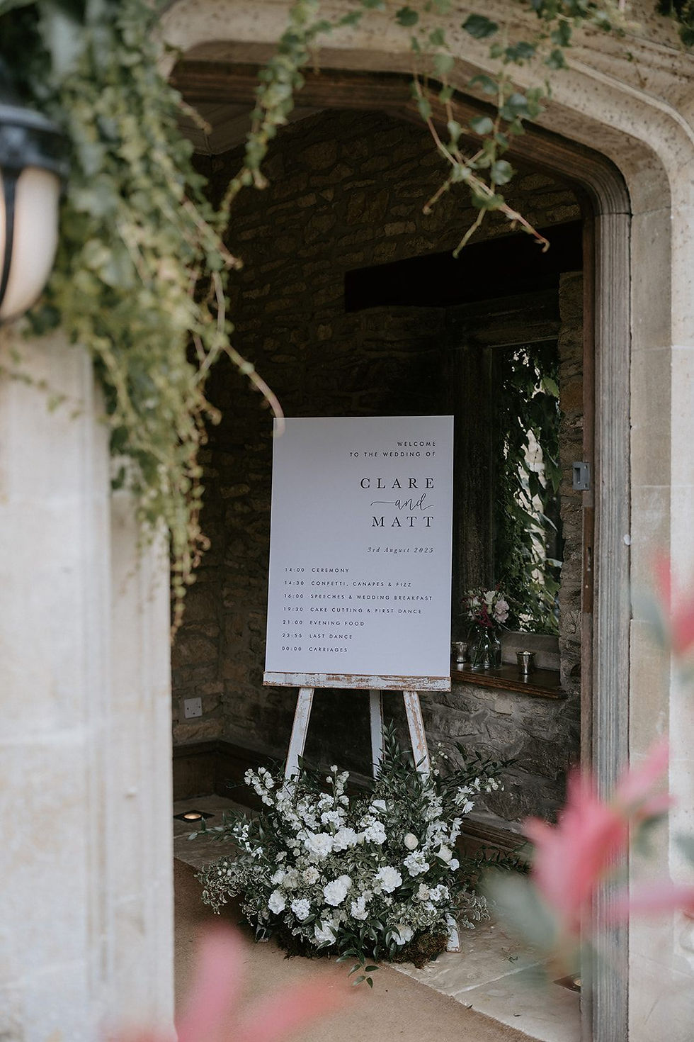 A monochrome wedding welcome and order of events combined sign placed on an easel at the entrance of a wedding venue