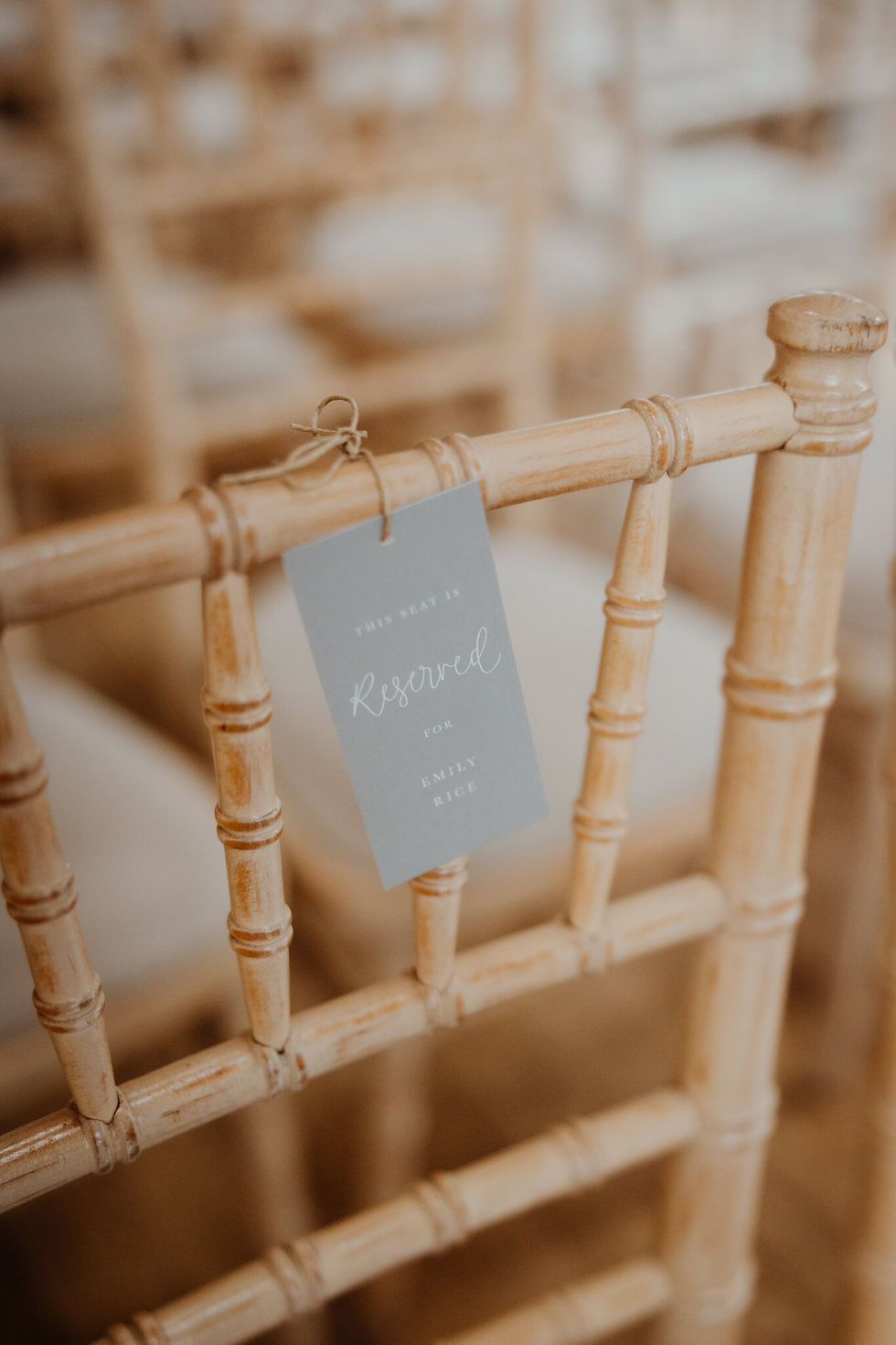 A ams, pale green reserved tag with white calligraphy, tied to a chair at the front of the wedding ceremony