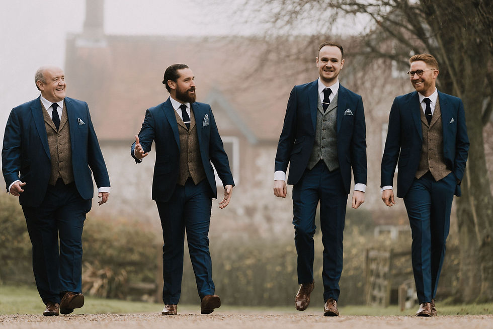 The groom and groomsmen walk outside in their matching navy suits with a grey waistcoat for the groom and pale brown waistcoat for the groomsmen.