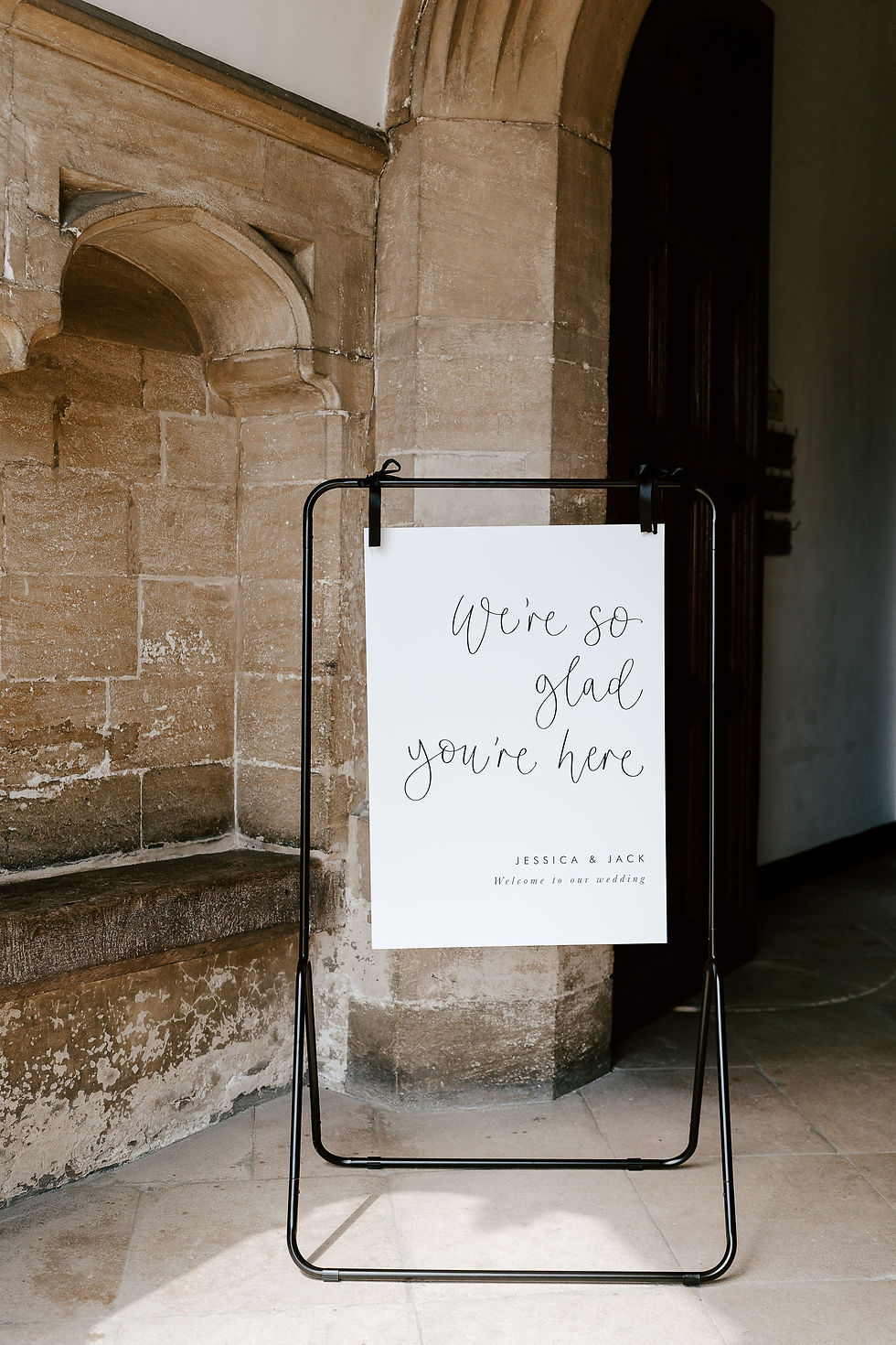 A stylish wedding welcome sign with black calligraphy on white card, tied with black bows to a black easel