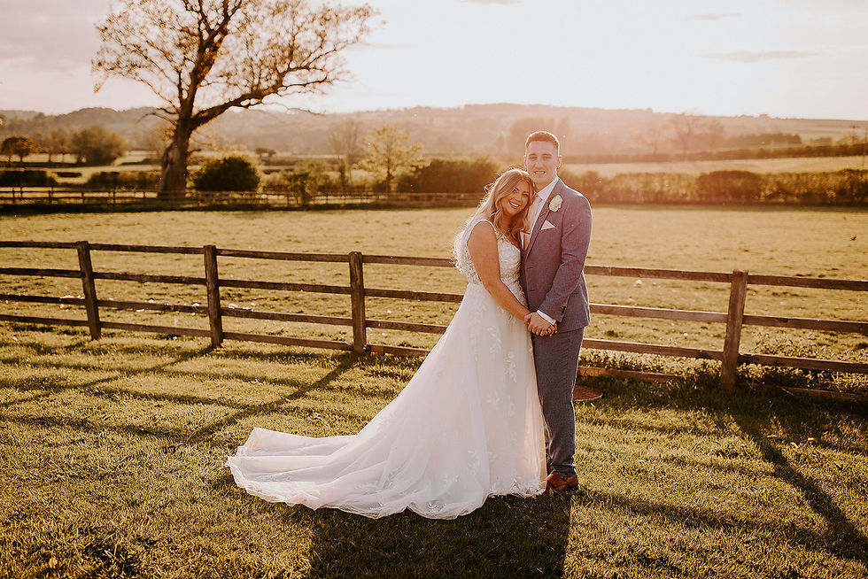 The bride leans into the groom as they pose outside in the grounds of the wedding venue