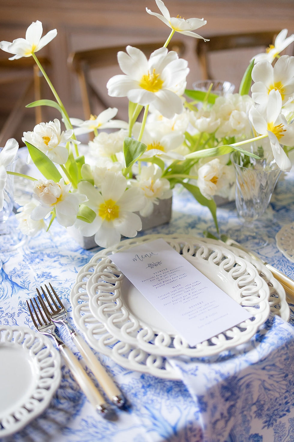 A wedding menu on pale blue card with a floral illustration and touches of calligraphy laid on a statement lattice plate and english countryside inspired blue and white linen.