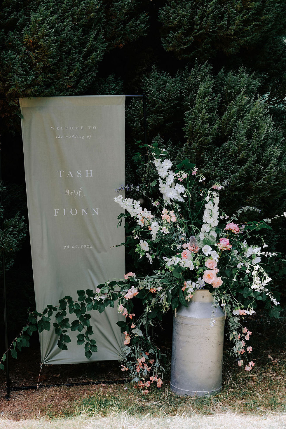 A sage green wedding welcome sign with white ink, styled next to pastel florals