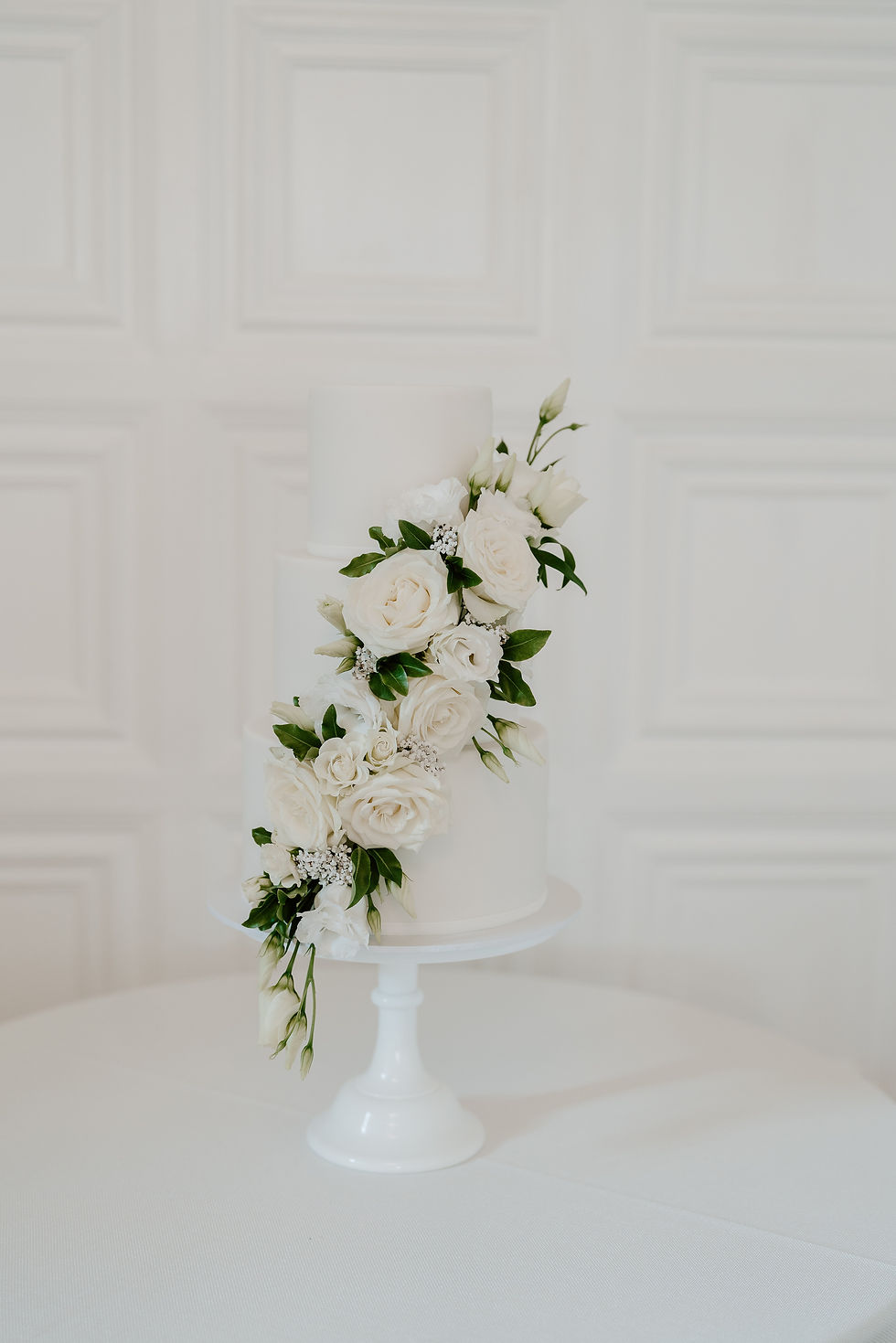 An iced white wedding cake decorated with cream roses and foliage