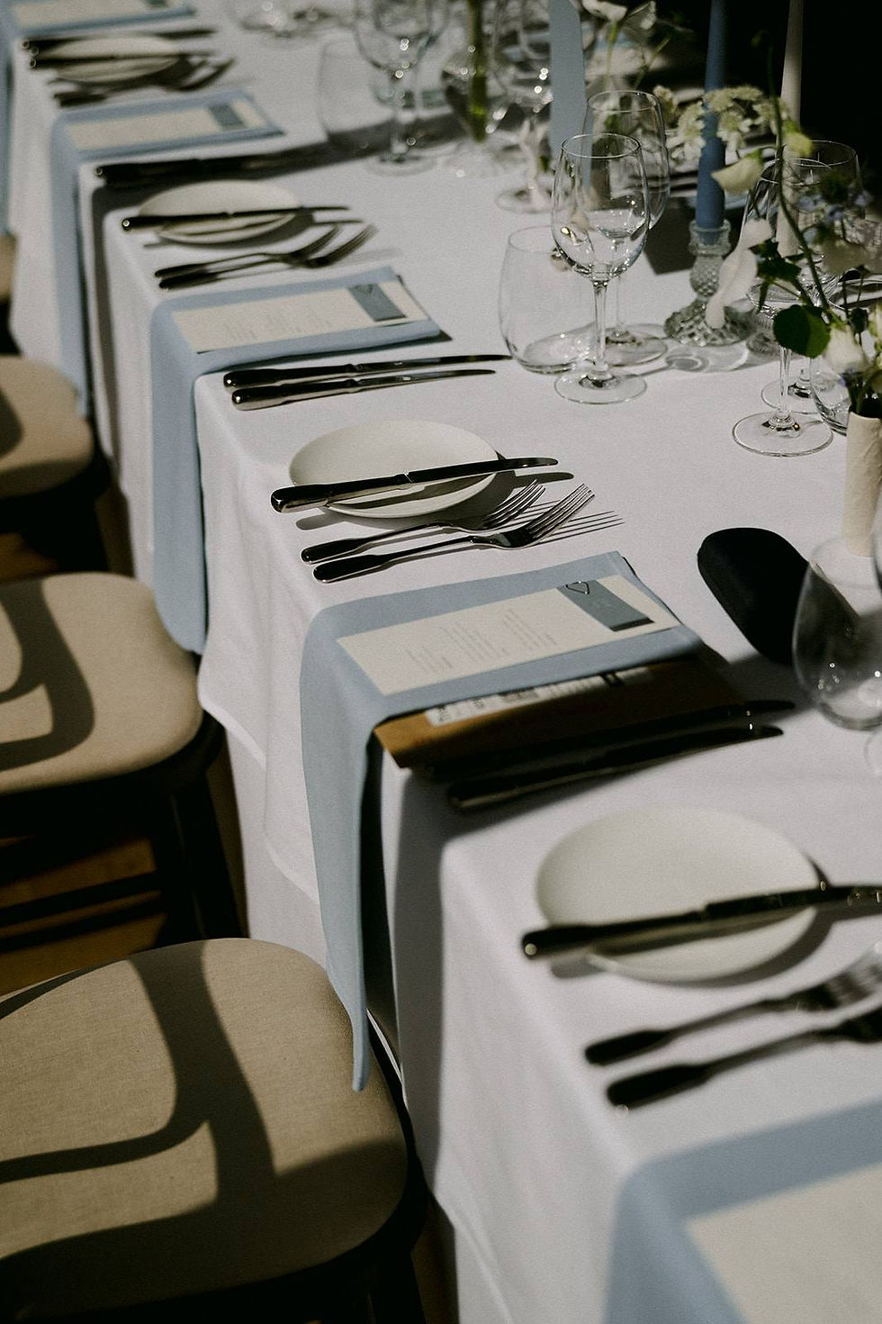 A wedding breakfast layout with pale blue napkins and guest names, white wedding menus, pale blue candles and small floral arrangements