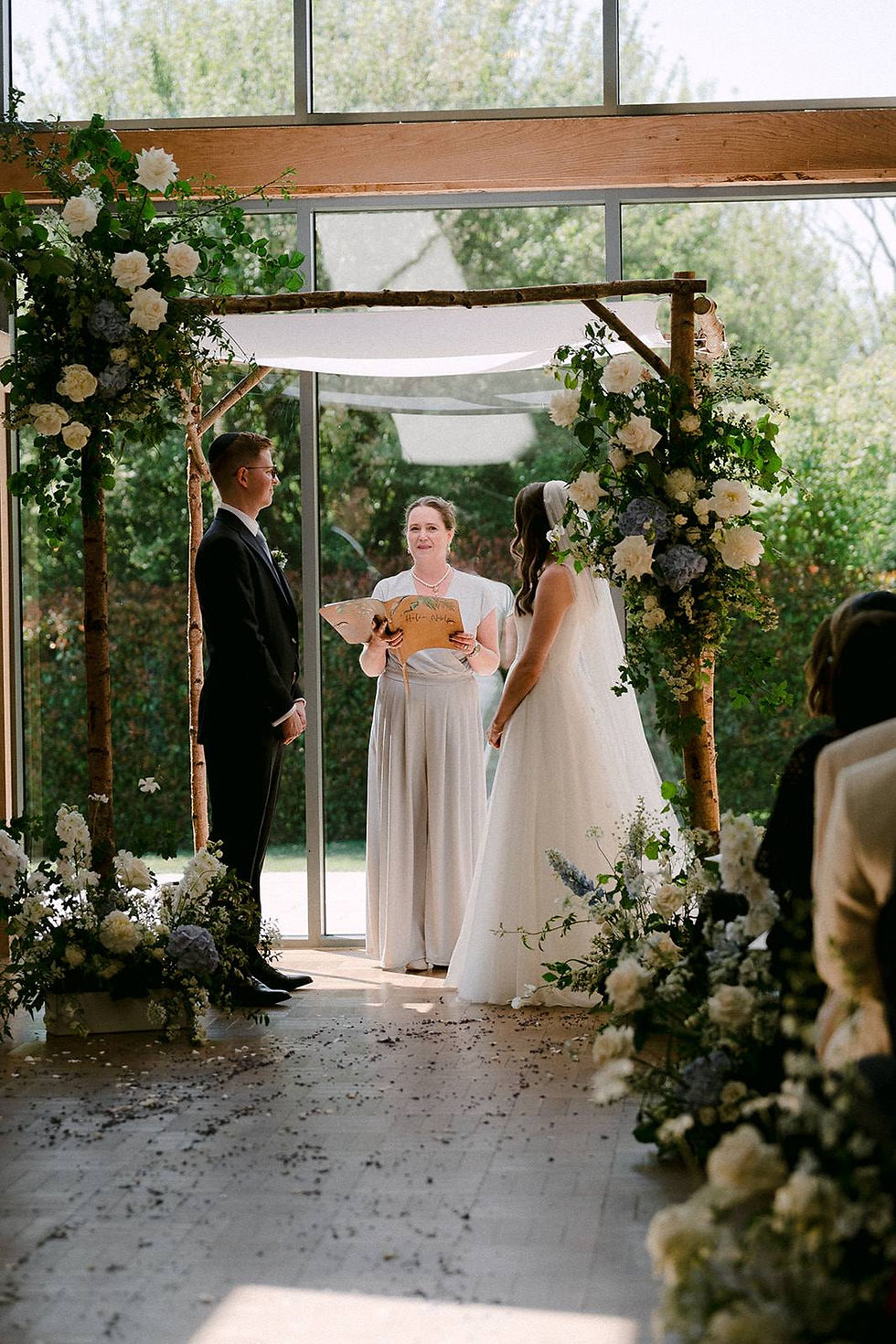 A bride, groom and chuppah standing as part of their ceremony surrounded by flowers