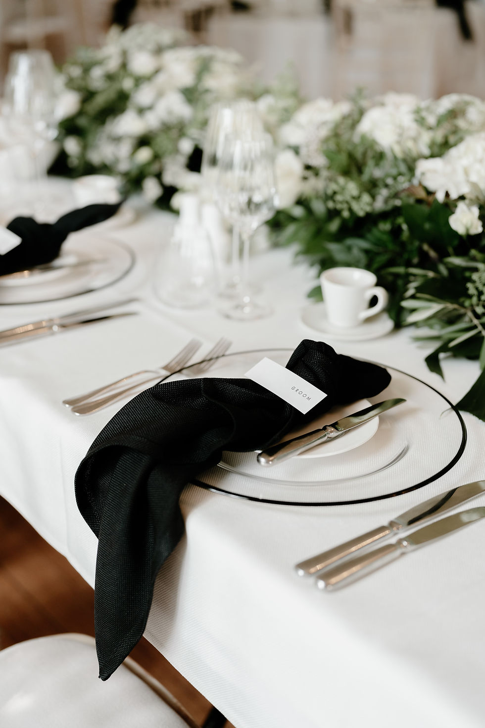 A wedding guest place name with black text on white card, layered on a black napkin