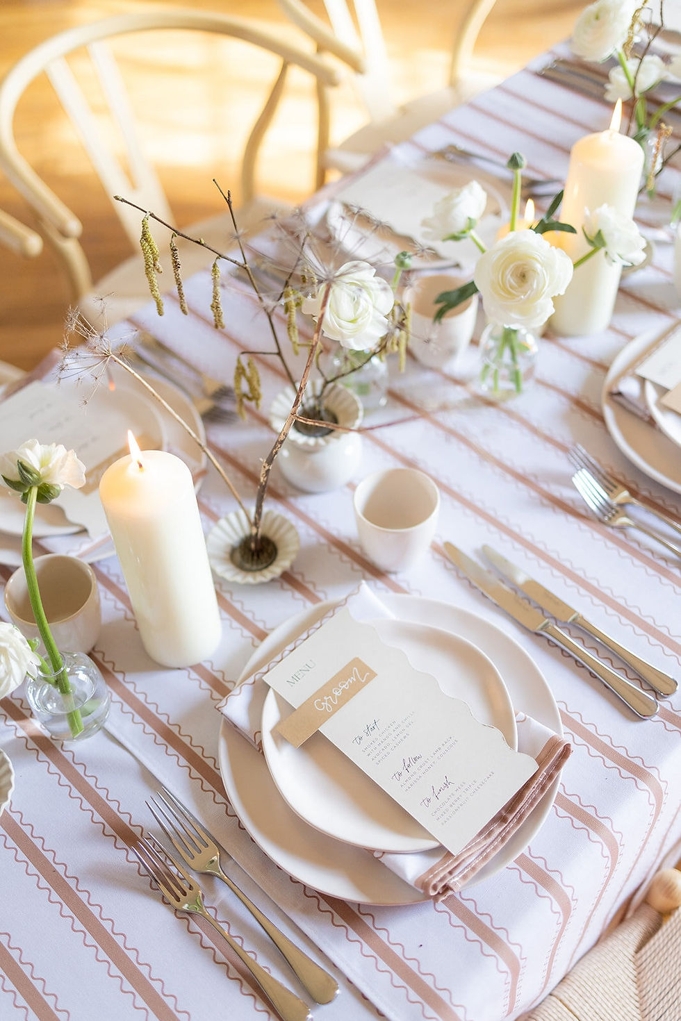 A wedding table set up with a patterned tan and white luxury table cloth, cream crockery, cream candles and silver cutlery.