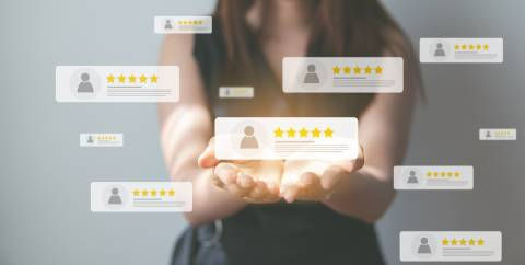 Person holding out hands with floating digital review icons displaying user profiles and five-star ratings, symbolising customer feedback or testimonials.