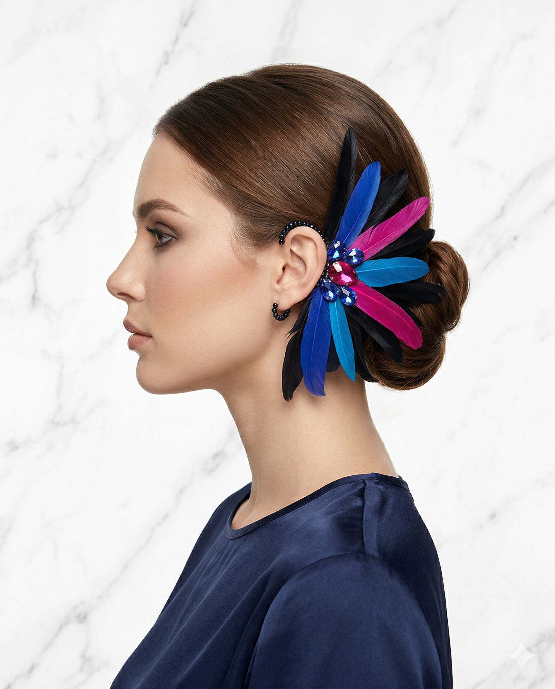 Ear cuff artesanal de luxo modelo Íris, com penas em azul, rosa e preto e cristais brilhantes, fotografado sobre fundo de már