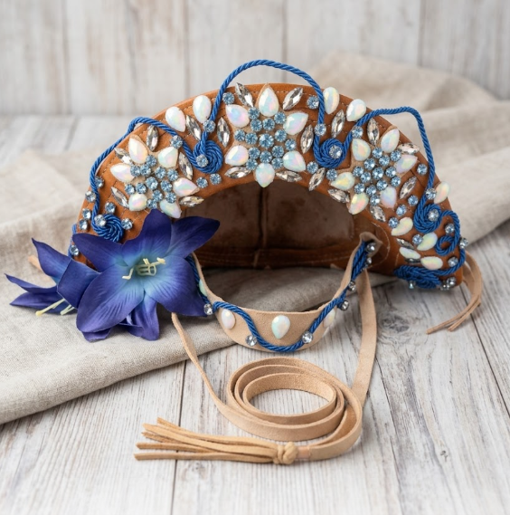 Foto de um chapéu de couro artesanal marrom decorado com pedrarias azuis e brancas, cordões azuis trançados e uma grande flor