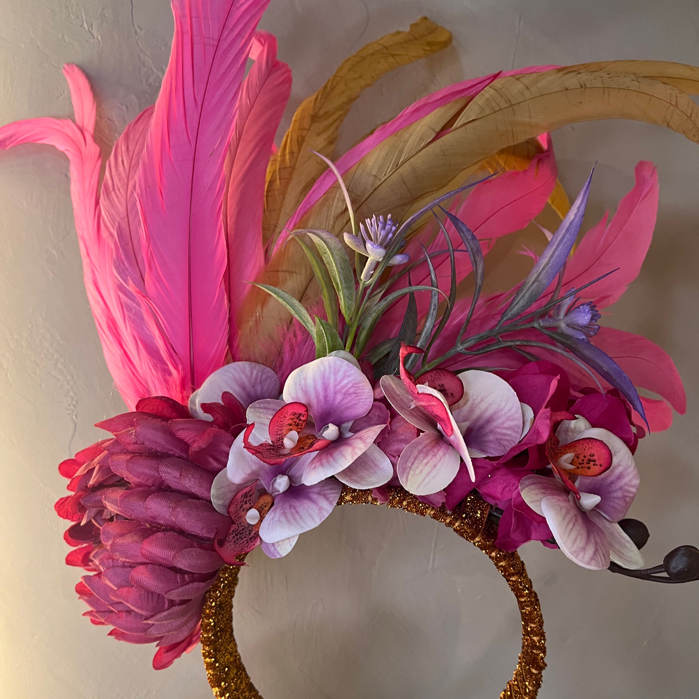 "Tiara de Carnaval luxuosa com arranjo lateral de orquídeas rosas e brancas, uma flor grande bordô e plumas altas em tons de