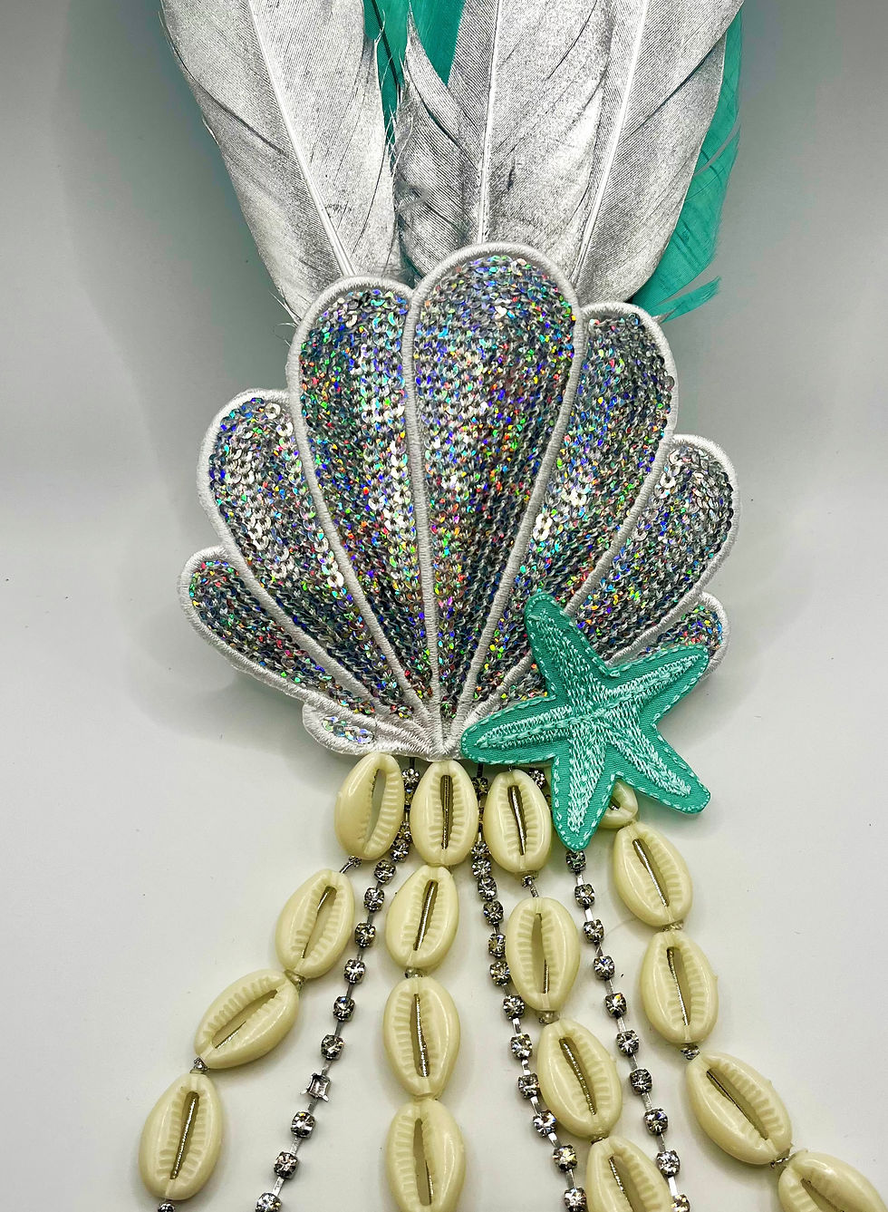 Presilha com concha prateada, penas pratas e verde água. Com Buzios e Strass caindo.