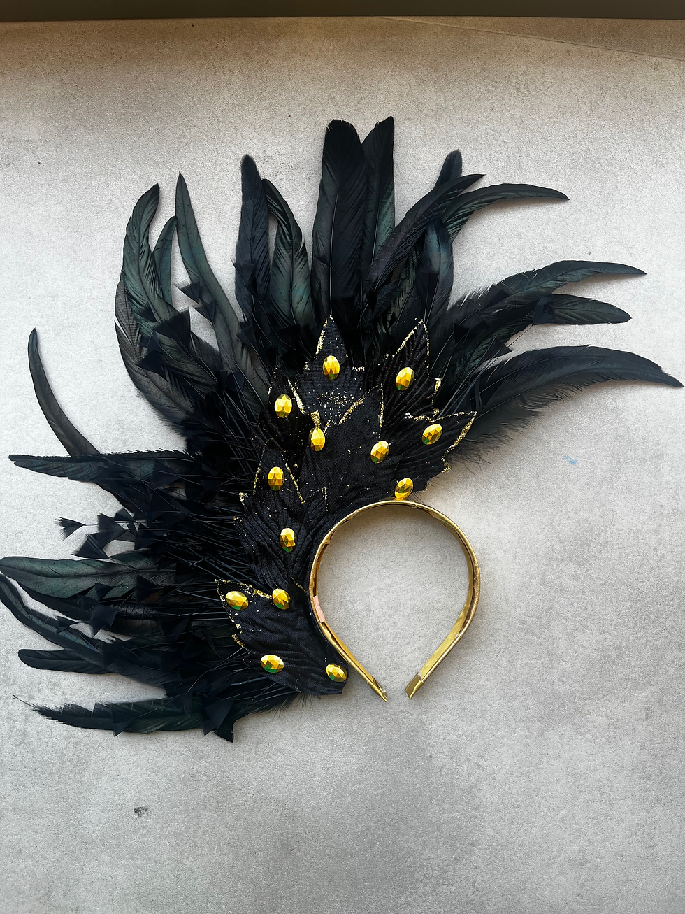 “Tiara lateralizada de Carnaval com folhas negras e douradas, penas pretas e pedras douradas decorativas.”