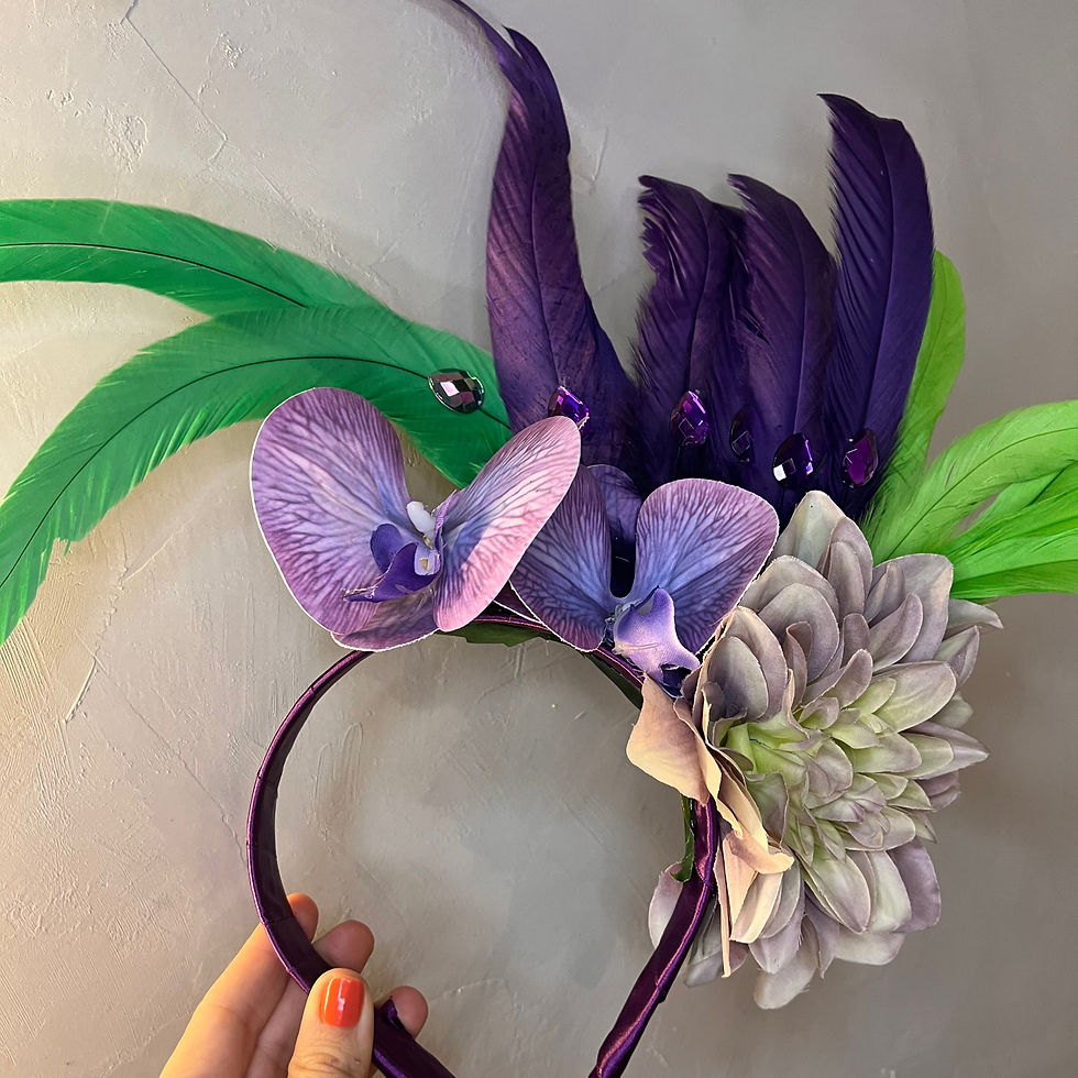 "Tiara de luxo com arranjo lateral de orquídeas roxas, flores verdes e penas em tons de roxo e verde."