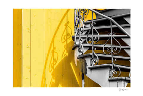 Photo laissant paraître une partie d'un escalier montréalais en noir et blanc sur un mur jaune.