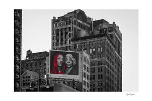 Duo de femmes sur un panneau publicitaire dont l’une se distingue en rouge sur un fond noir et blanc.