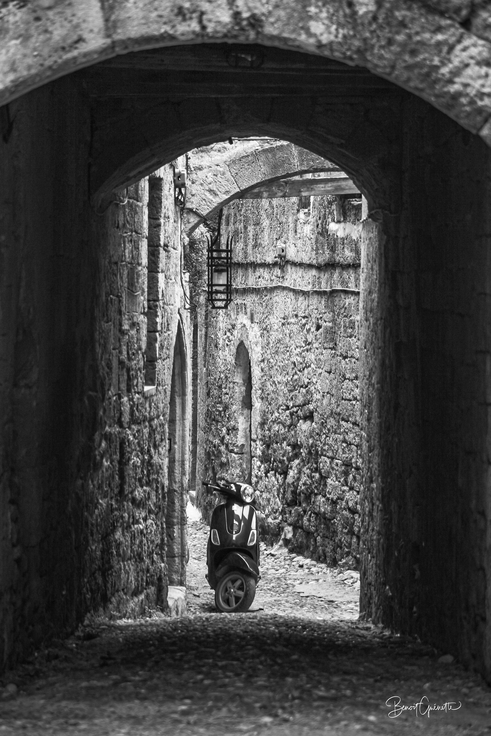 Un cyclomoteur repose sous une arche de pierre, seul dans une ruelle étroite de la vieille ville