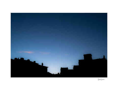 Image couleur de la silhouette de bâtiments de la Piazza dell'Anfiteatro à Lucca se découpant sur un ciel bleu.