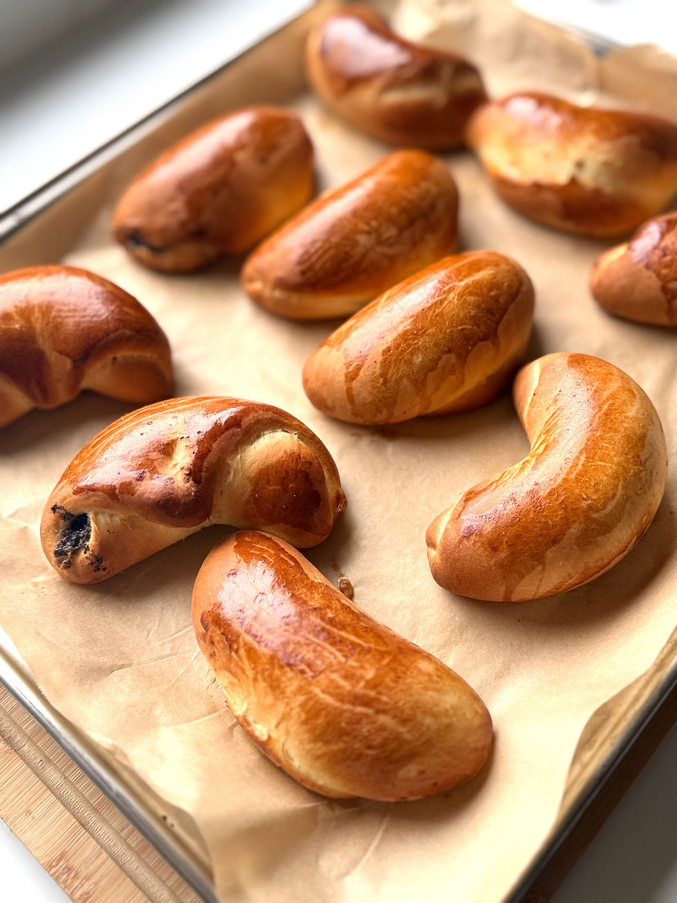 Tray of freshly baked golden-brown Hungarian mákos kifli on parchment paper.