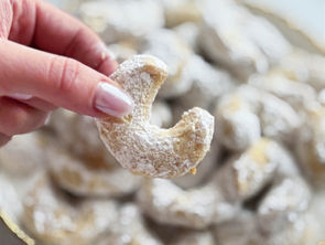 A hand holding a powdered sugar–coated walnut vanilla crescent cookie above a plate filled with more Hungarian vaníliás kifli.