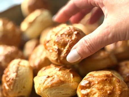 Hand picking up a freshly baked Hungarian cheese pogácsa from a pile of golden homemade savory pastries.