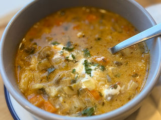 Hungarian mushroom soup with butter dumplings, carrots, mushrooms, sour cream and fresh parsley in a grey bowl.