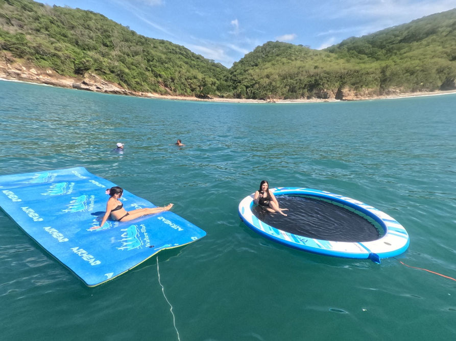 Guests on a floating water mat and water hammock in a green bay on a Punta Mita yacht charter