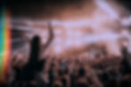 Outdoor concert crowd with people enjoying the performance, including a woman being lifted on someone’s shoulders and individ
