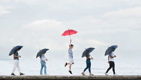 Junge Menschen gehend mit grauen Regenschirmen, ein Mann mit rotem Regenschirm springend