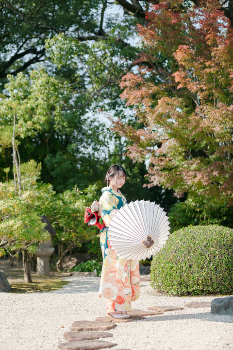 日本庭園で白い和傘をさしかけている振り袖を着た女性