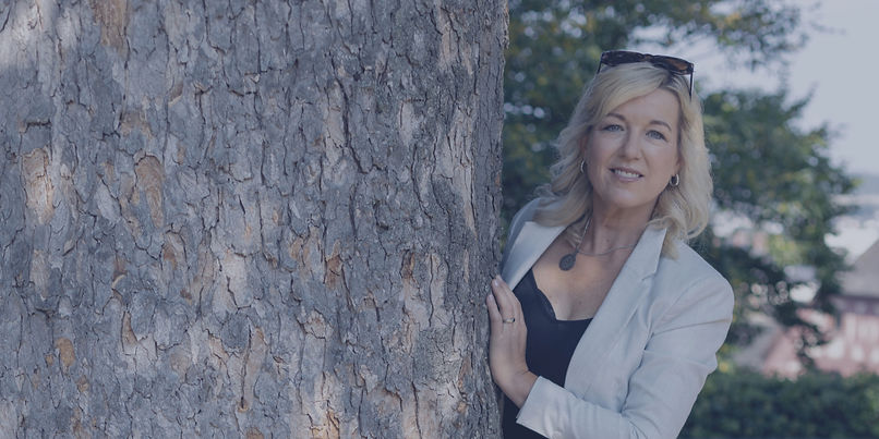 Andrea Durig lehnt an einem Baum in der Natur