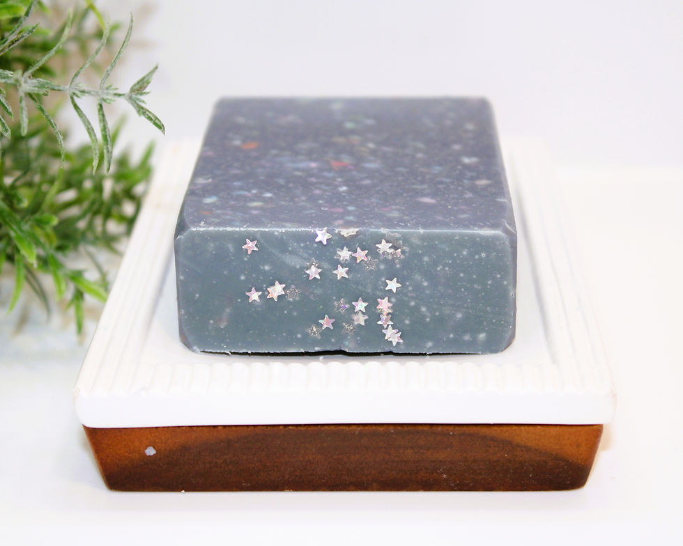Deep greyish blue confetti soap bar with star glitter on white soap dish with greenery background
