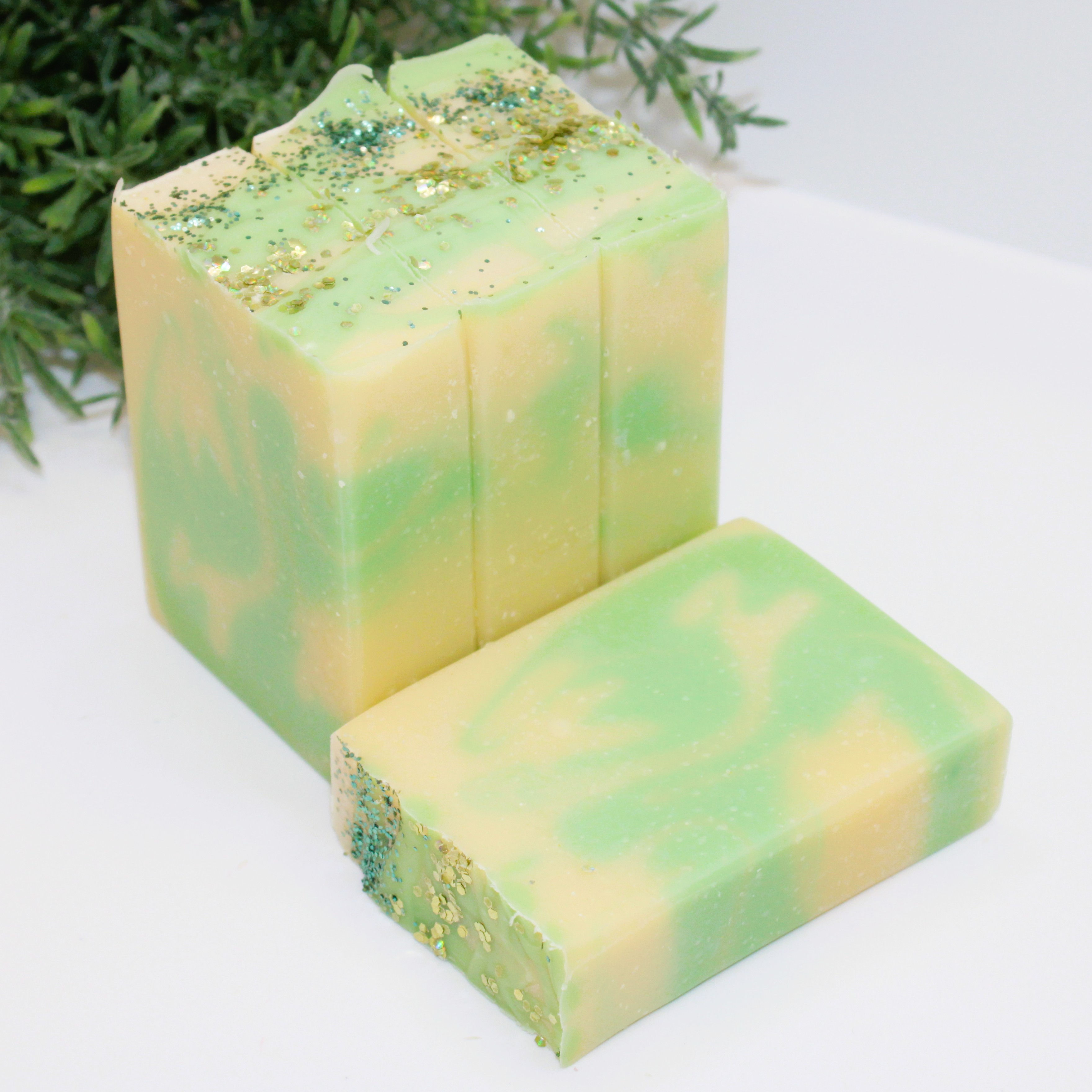 Green and yellow soap bars standing in a row, one soap laying flat on a white surface, with white and greeneary background