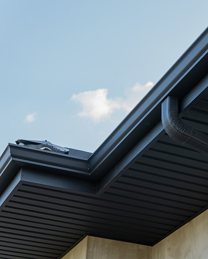 Close view of a roof edge and downspout against a bright blue sky highlights contemporary