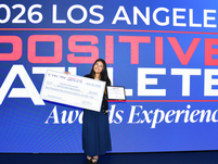 Smiling young woman holds a $2,500 check and award plaque onstage before a 2026 Los Angeles Positive Athlete Awards Experience backdrop.