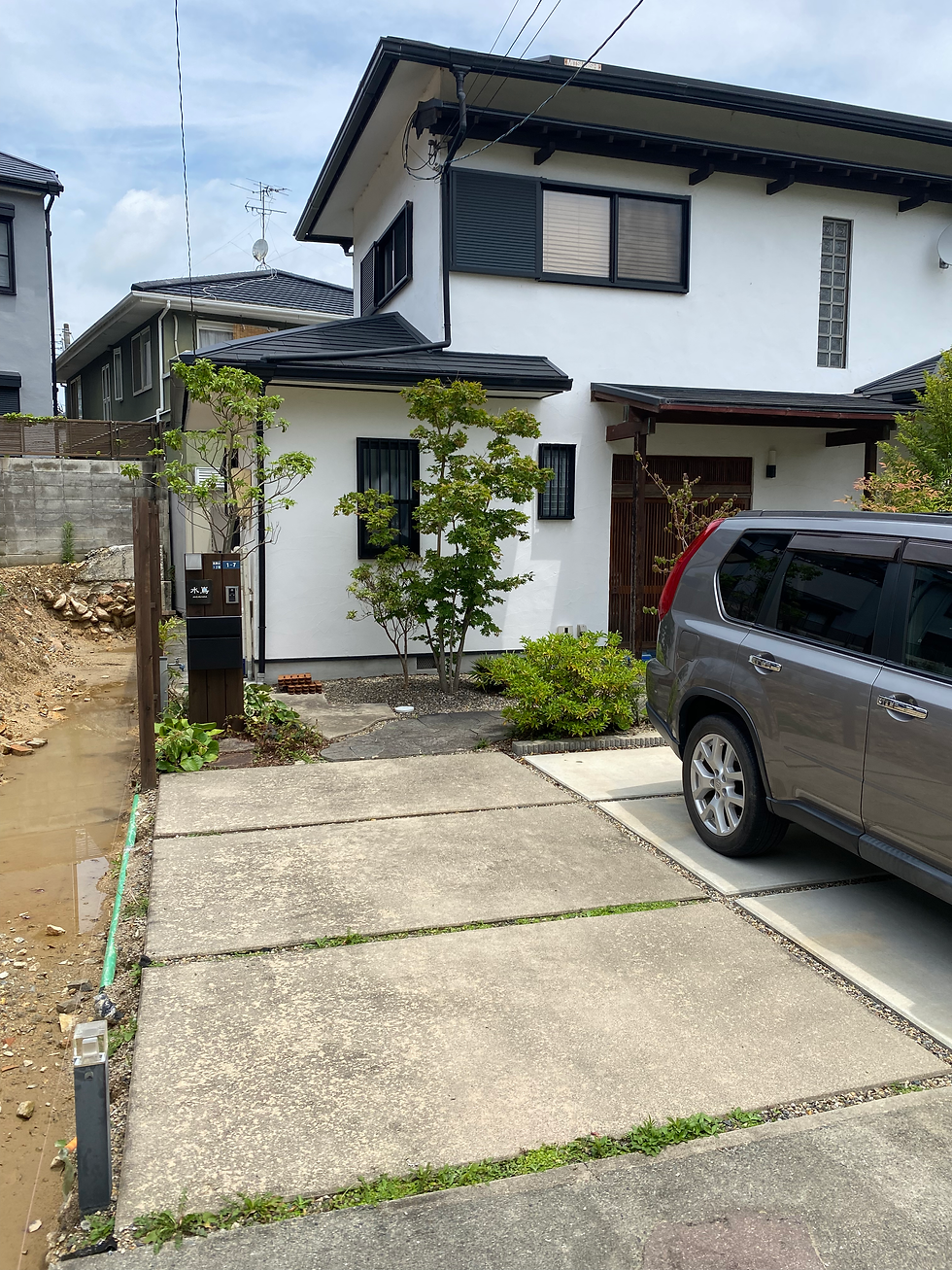 宝塚市の白いモダンな家と車、自然の庭の木々と未舗装の地面