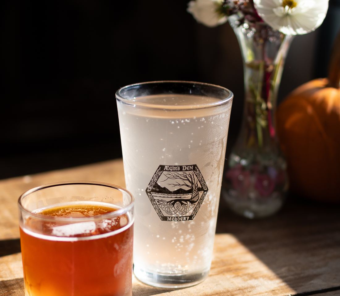 A pour of amber mead next to an Ægir's Den logo pint glass