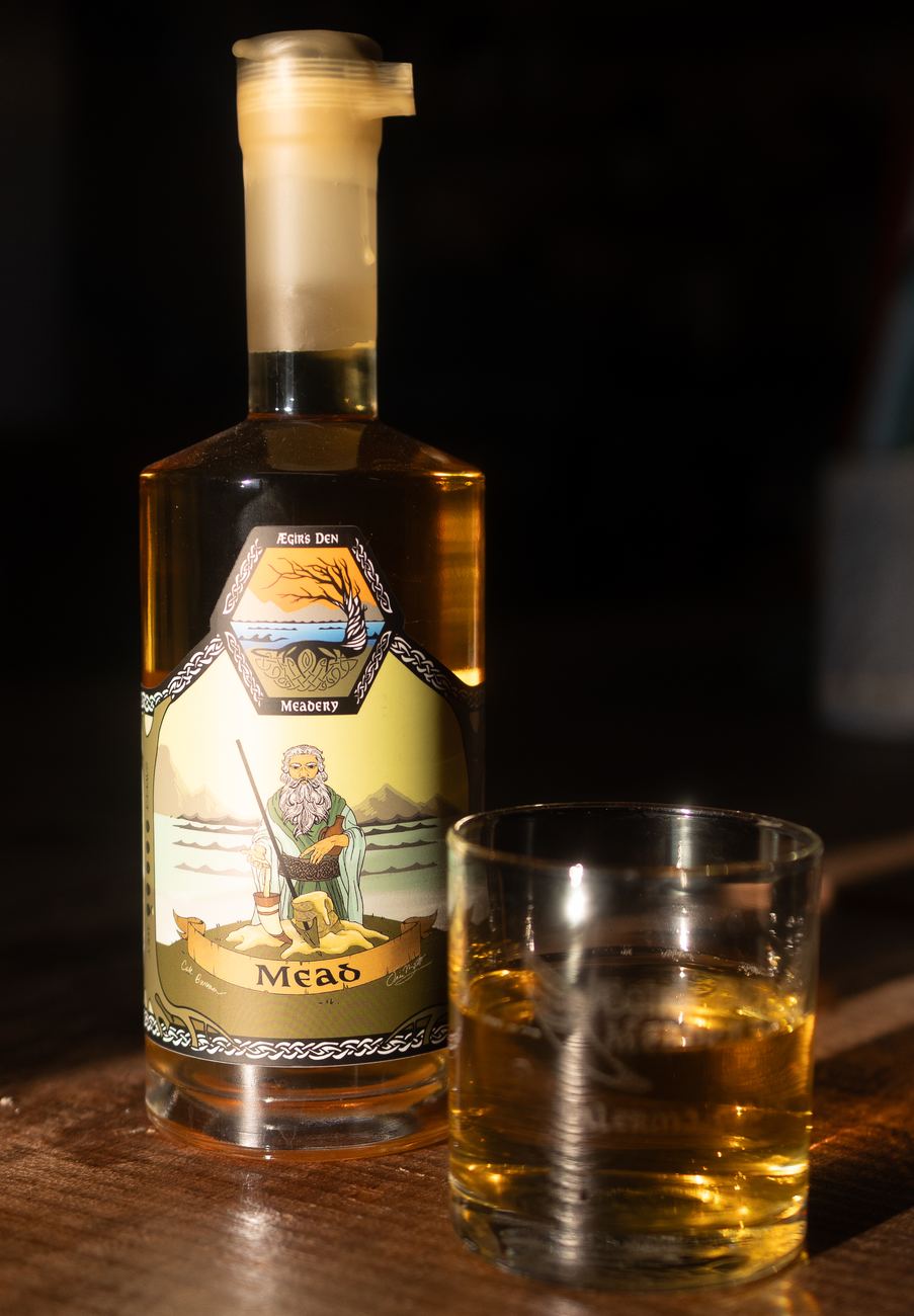 A bottle of Ægir's Den mead beside a poured glass on a dark wooden bar