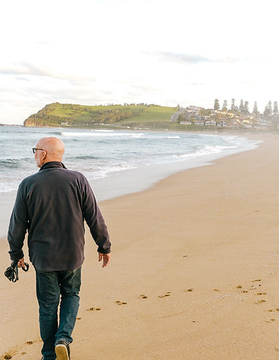 A man walking along Werri Beach in Gerringong with the headland and ocean in the background