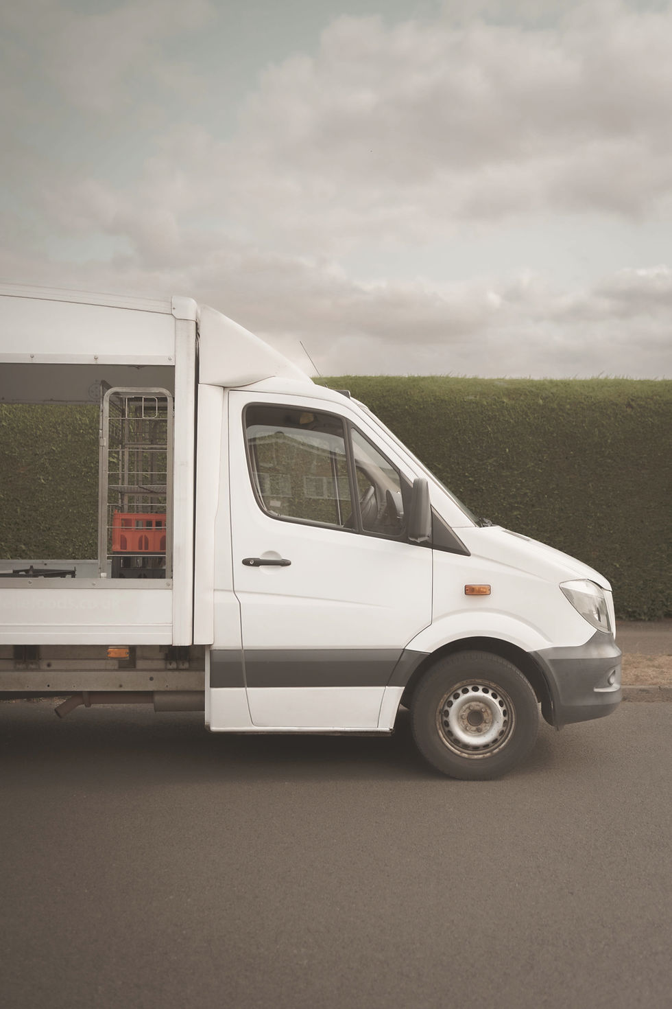 White milk delivery van with green hedge behind
