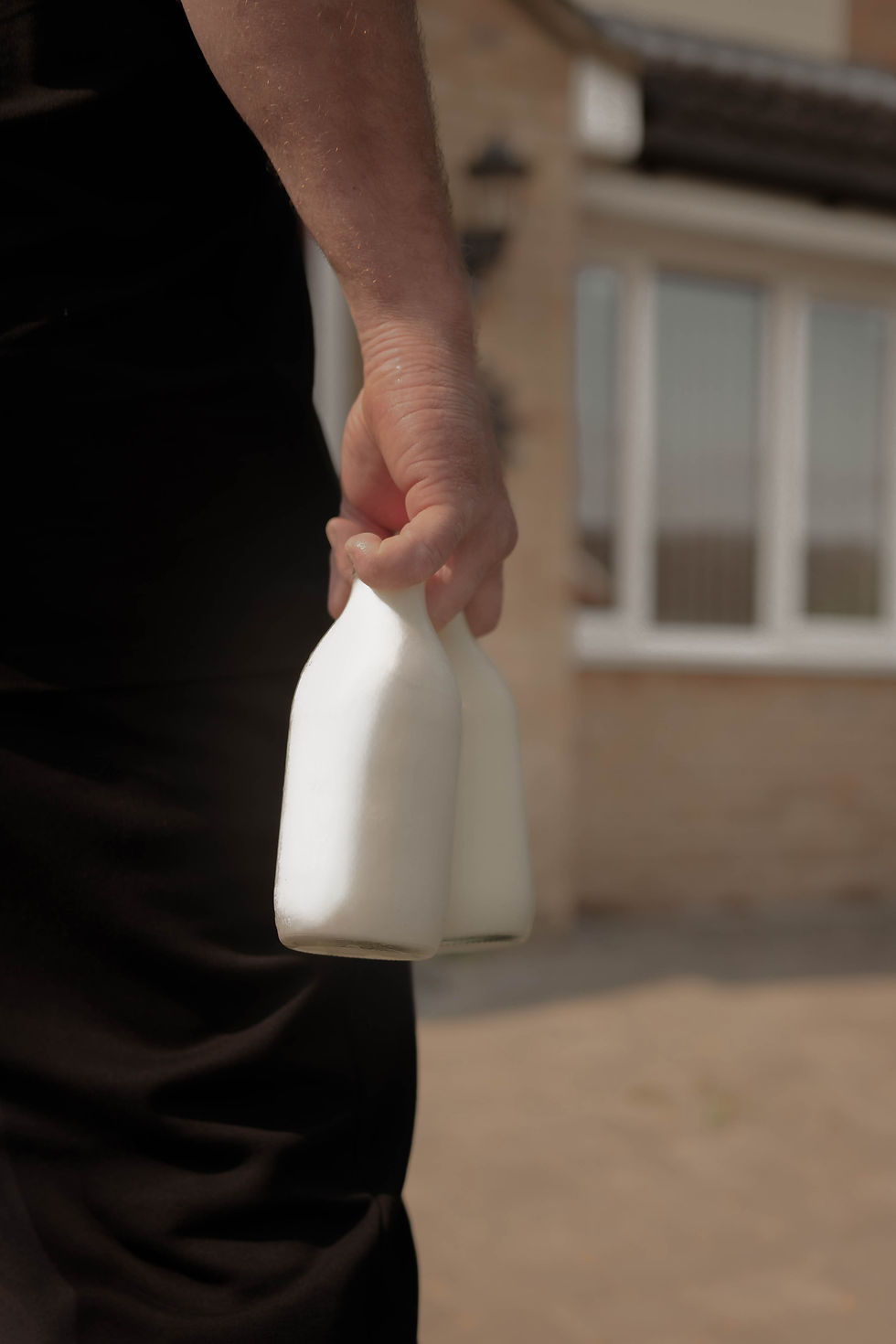 Hand carrying a glass bottle of milk to a doorstep.