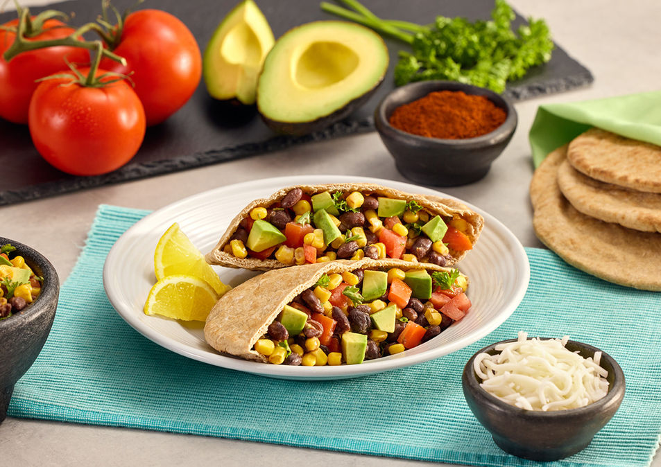 A vibrant plate of stuffed pitas with black beans, corn, avocado, and tomatoes. Beside it are fresh tomatoes, avocado, and spices, conveying a fresh, inviting meal.