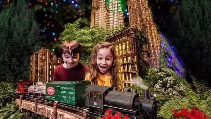 Children watching a model train pass through a miniature city display at the Holiday Train Show at the New York Botanical Garden.