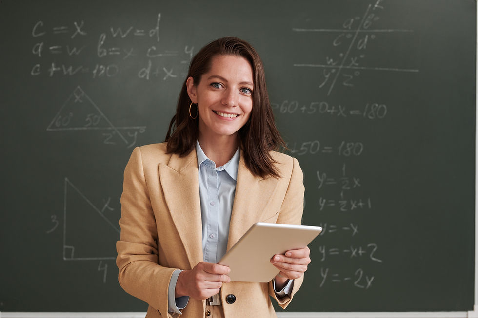 Math teacher stands smiling in front of a chalk board for parent teacher conferences.